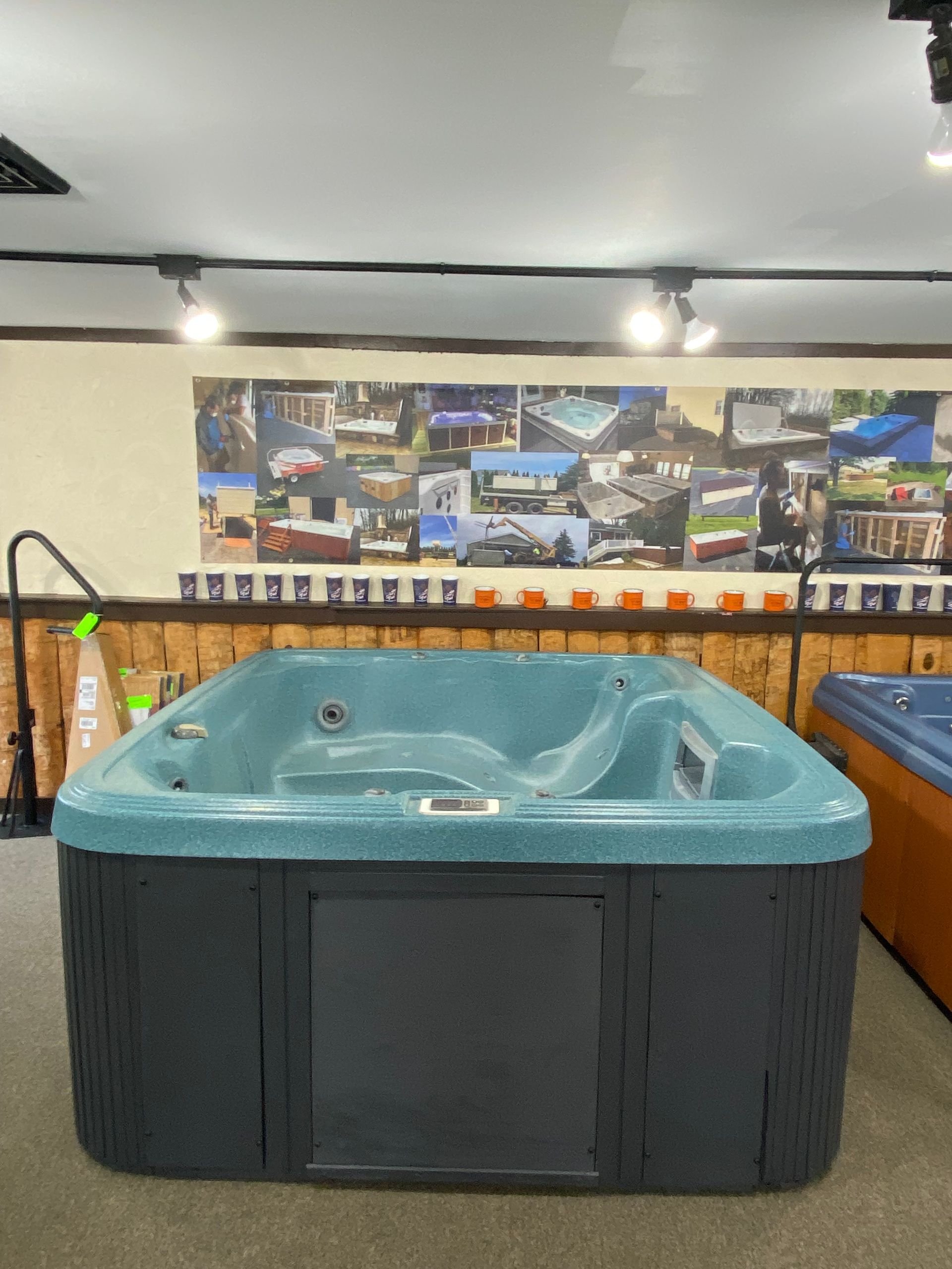 A blue and gray hot tub on display in a showroom, with a wood-paneled wall and product display in the background.
