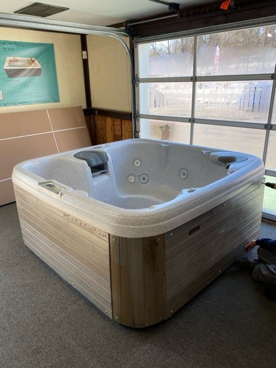 Hot tub with light brown wood paneling sits inside a garage with glass door.