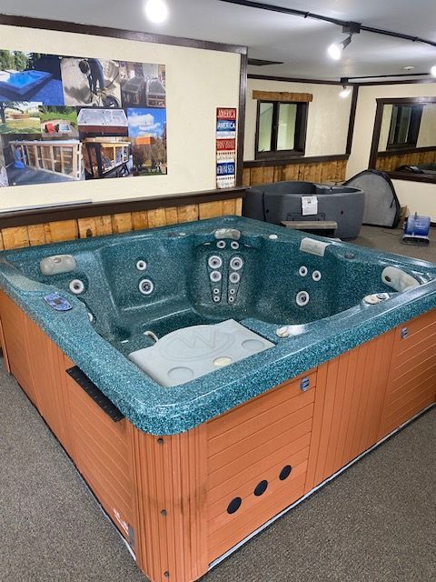 Large, turquoise hot tub displayed in a showroom with brown trim, wood panels, and a poster on the wall.
