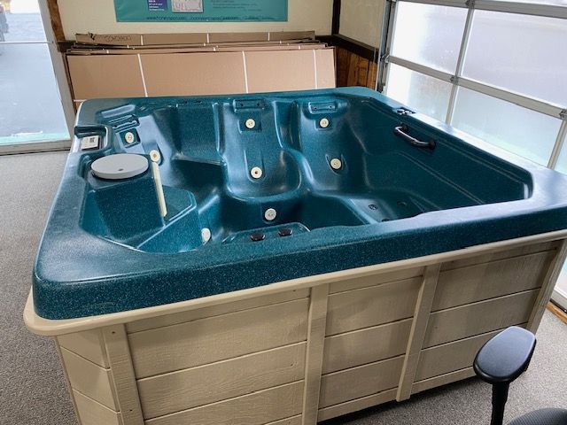 A teal hot tub with beige siding inside a building near a window.