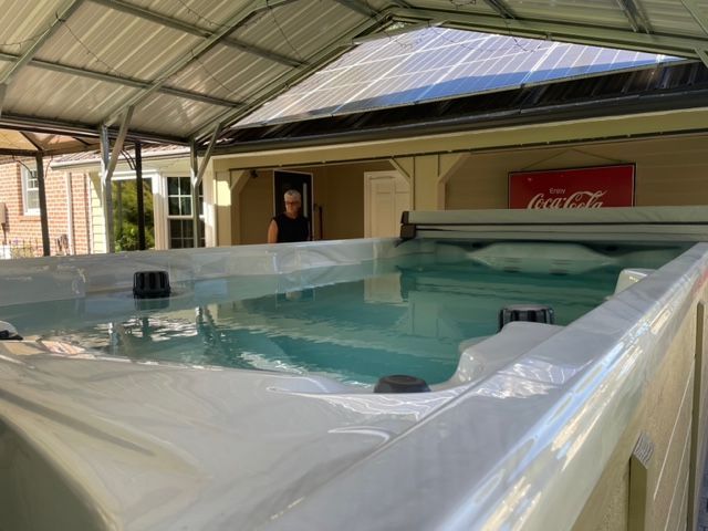 Swim spa under a carport with solar panels, a person in the background, and a Coca-Cola sign.