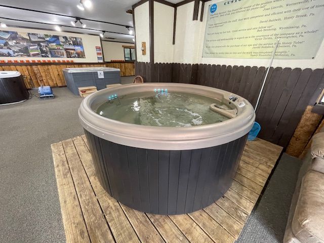 Round hot tub in showroom, gray exterior, tan trim, on wood platform.