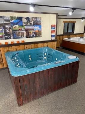 Square teal hot tub with brown wooden sides in a showroom.