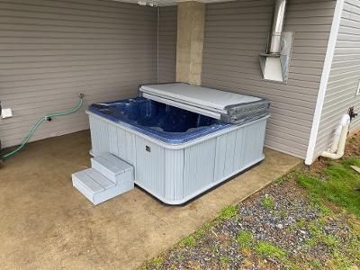 Hot tub with a cover and steps on a concrete patio next to a building.