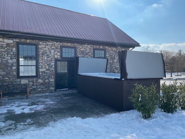 Hot tub next to a stone building with snow on the ground. Two covers are open.