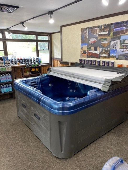 A hot tub on display in a store, with blue interior, gray exterior, and partially open cover.