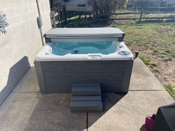 An outdoor hot tub with water filled and cover partially open on a concrete patio