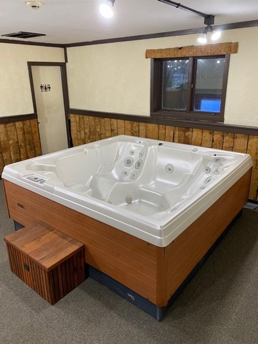 Hot tub in a room with wooden paneling, a step, and a window.