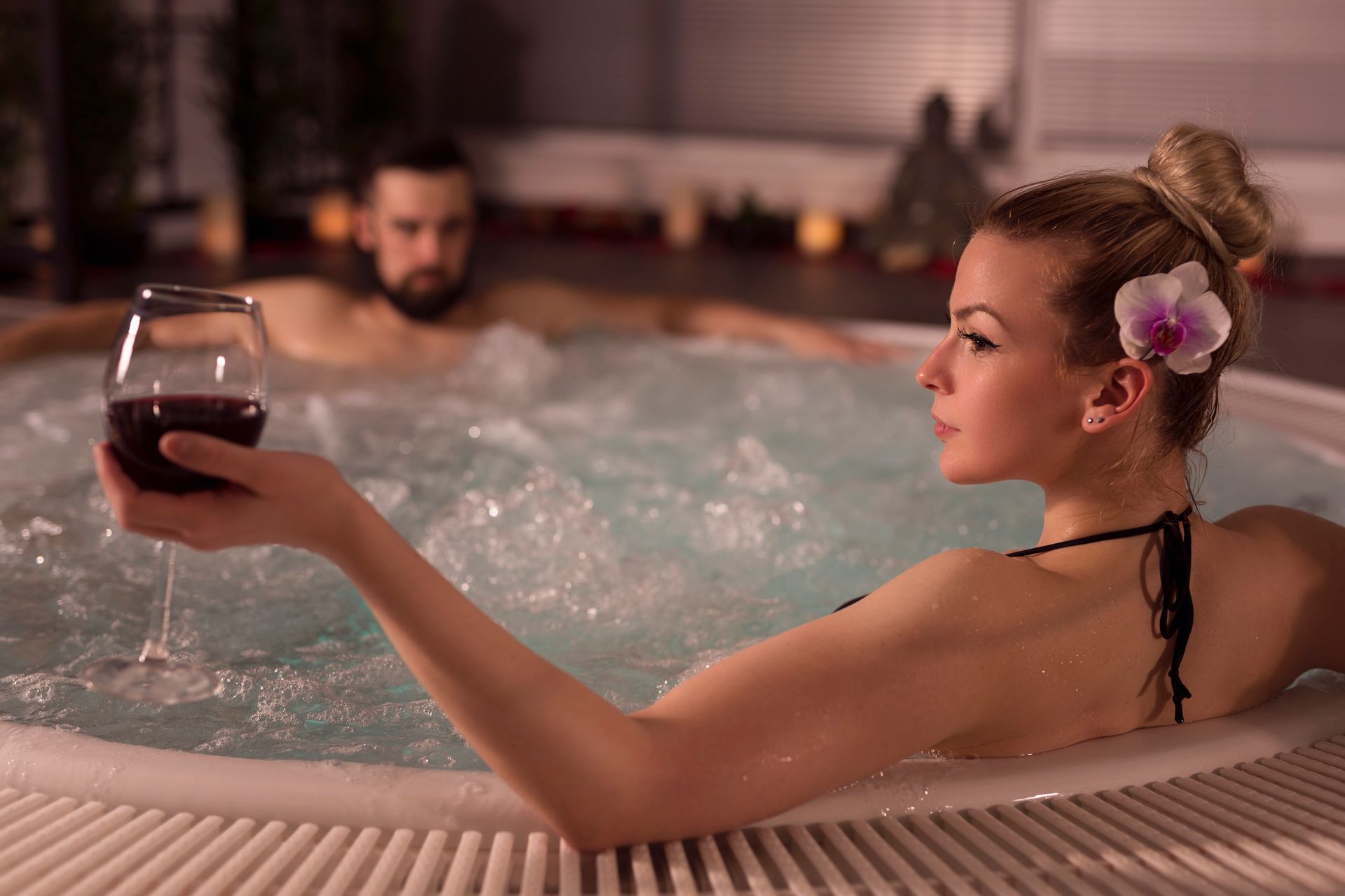 Person relaxing in a hot tub with a glass of wine during spa experience.