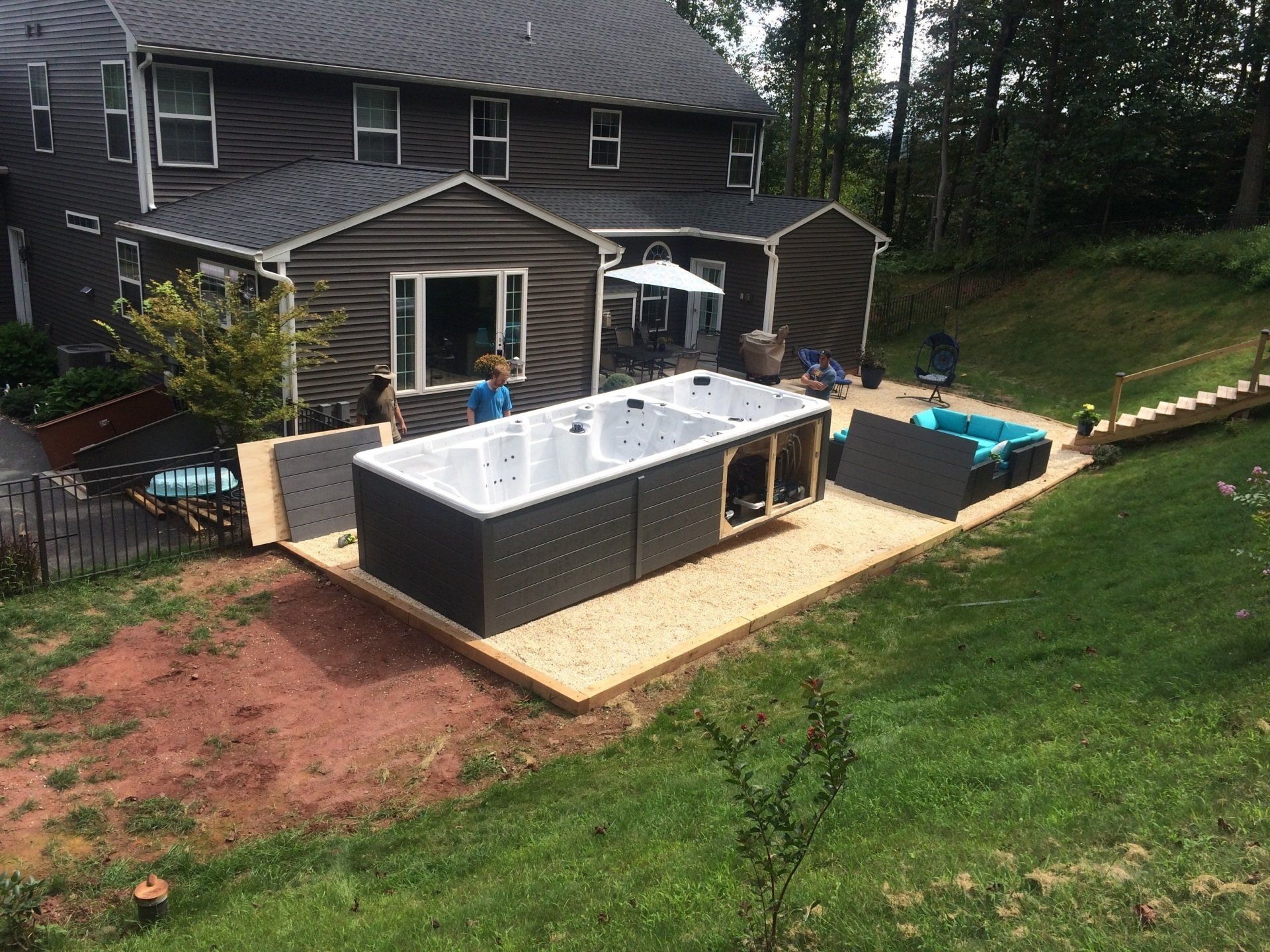 A backyard with a partially built swim spa on a gravel pad in front of a two-story house.