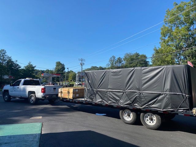 White pickup truck towing a trailer loaded with covered boxes in a sunny parking lot.