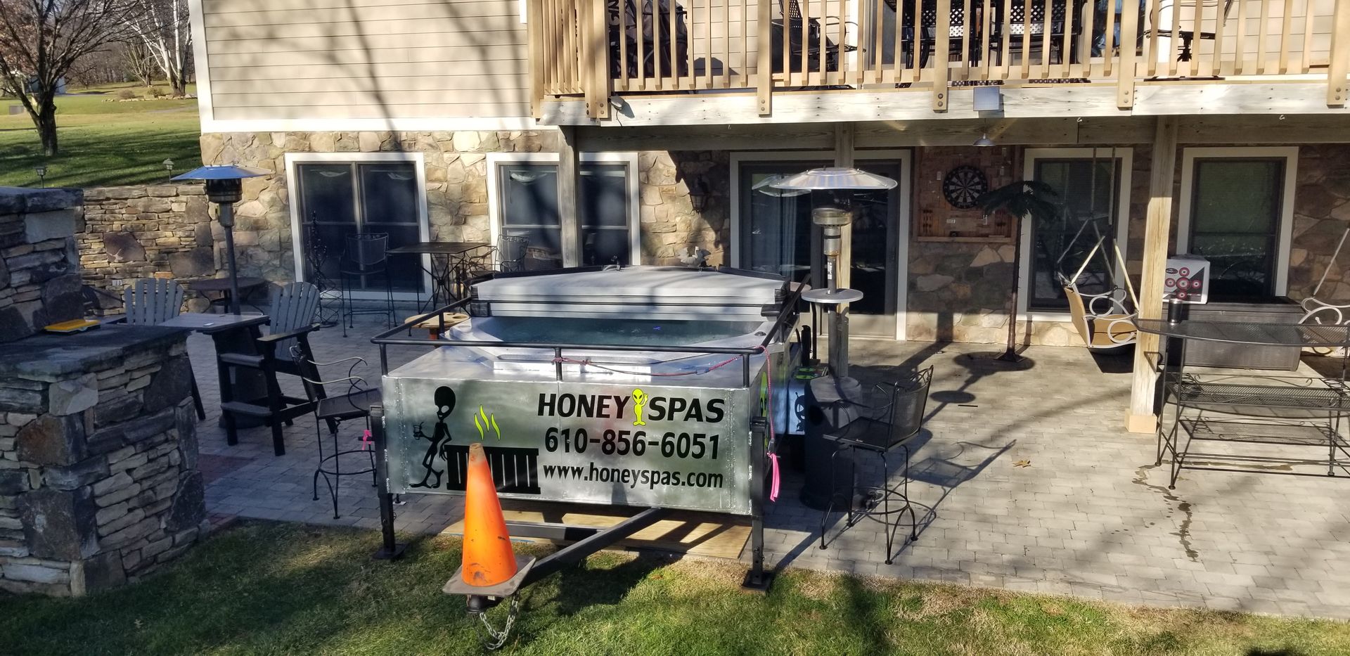 A hot tub on a trailer in front of a house. The tub has a cover and an orange traffic cone is in front.