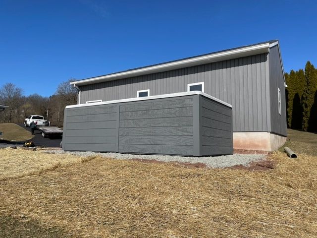 Gray storage unit next to a gray building on a sunny day, gravel foundation.
