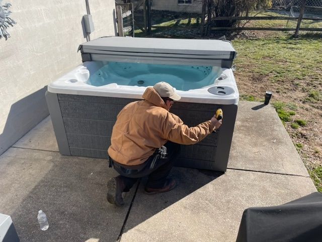 Man in a jacket kneels near a hot tub on a patio, possibly inspecting or repairing it.