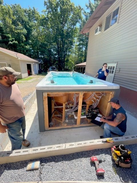 Three people working on a swim spa installation next to a house.