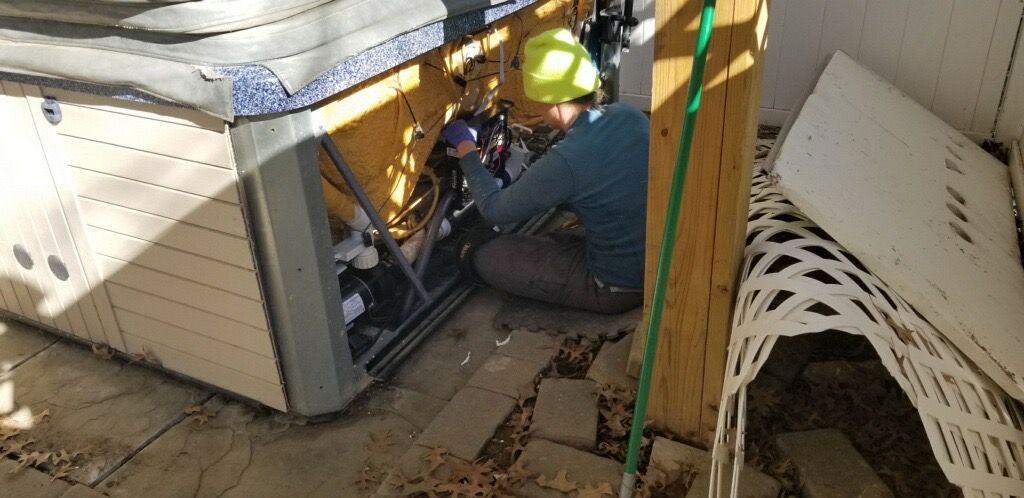 Person in yellow hard hat repairing hot tub.