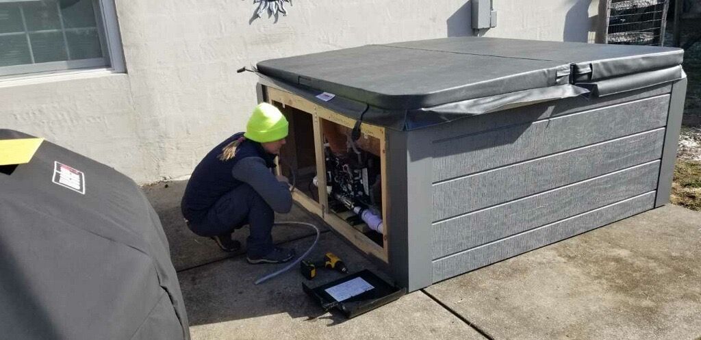 A person in a hard hat works on a hot tub outside a house.