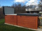 Outdoor hot tub with brown wood exterior and open gray cover.