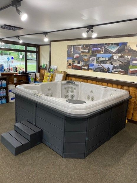 Hot tub display in a showroom with grey siding, steps, and white interior.