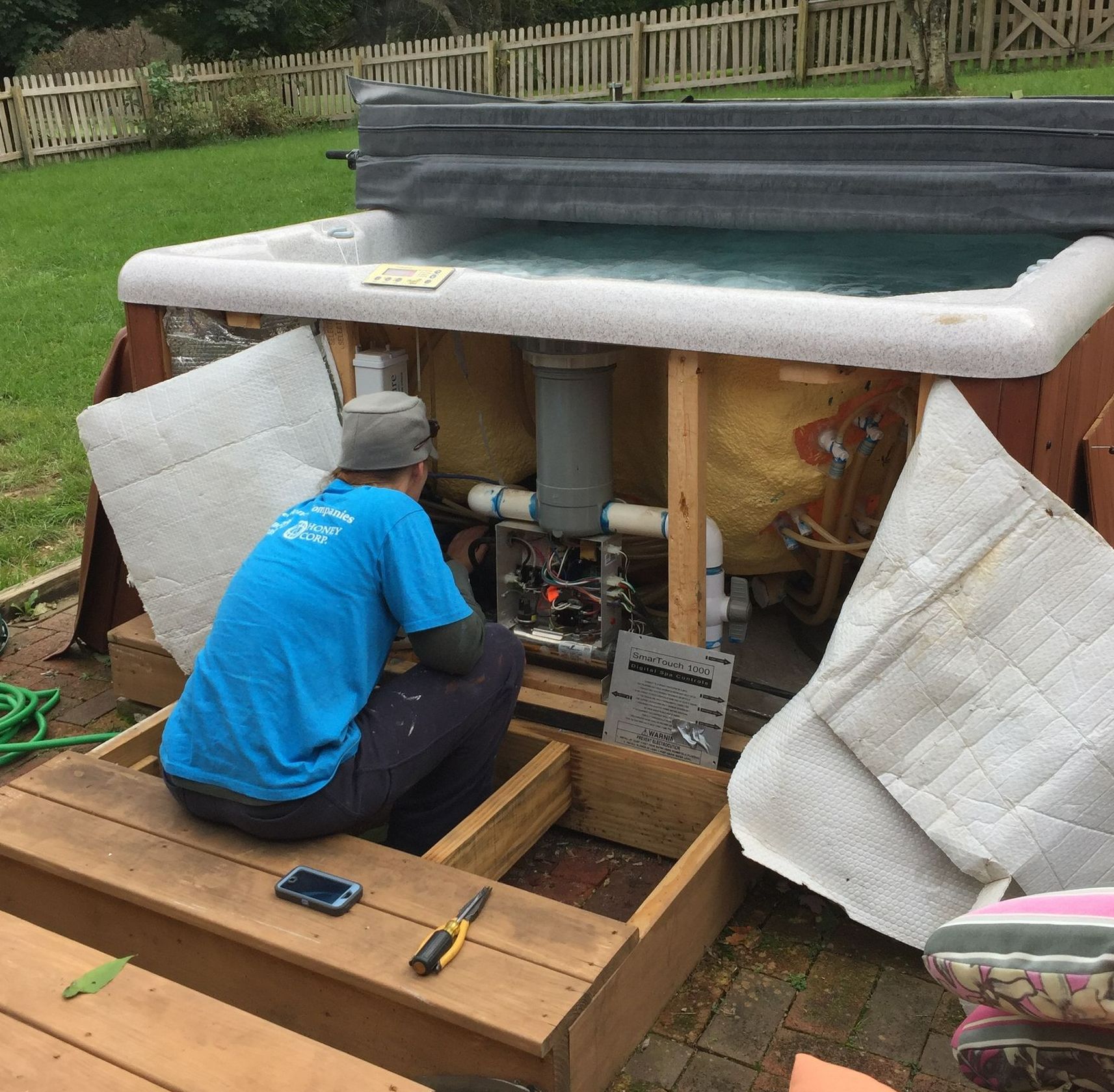 A man is working on a hot tub in a backyard.