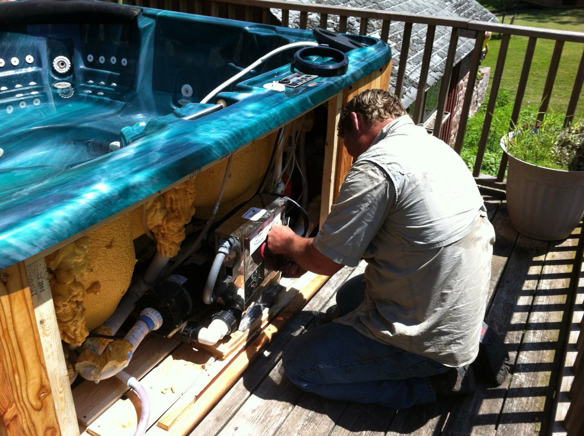 Man repairing hot tub pump on outdoor wooden deck.