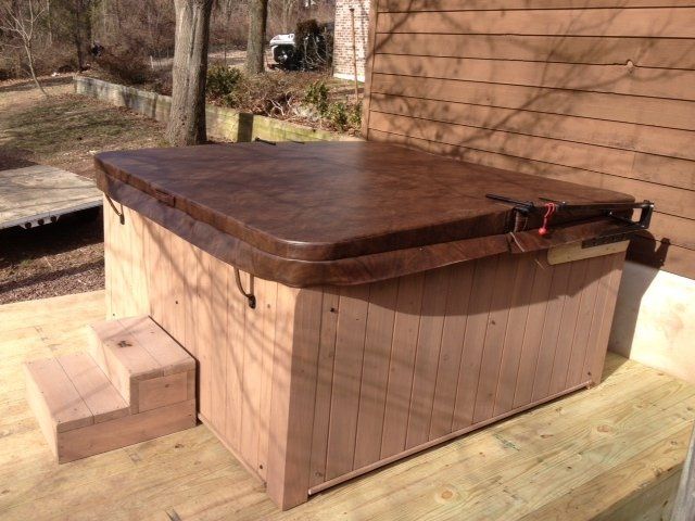 Hot tub with brown cover, wooden steps, and wooden exterior siding on a sunny deck.