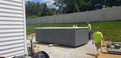 Three workers in yellow shirts near a gray rectangular structure outdoors, possibly installing it.