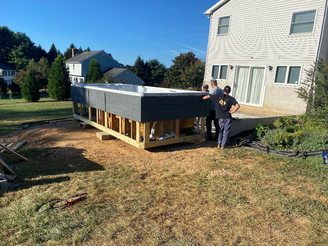 Three men building a rectangular above-ground pool structure on a grassy backyard next to a house.