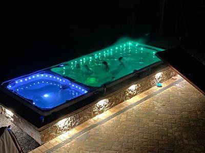 Night view of a dual hot tub with blue and green lights. People in the green tub. Brickwork surrounds.