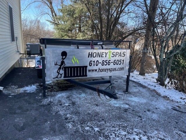 Honey Spas trailer with logo, parked on snowy asphalt near a house.