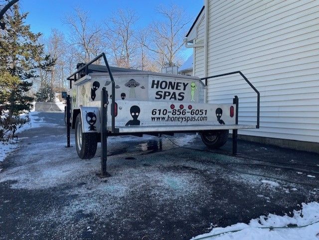 Trailer for Honey Spas, silver with alien logo and contact info parked on snowy asphalt near a house.