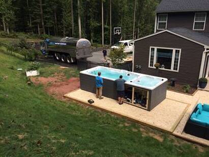 Two men working on a new dark grey swim spa next to a house. A water truck is in the background.