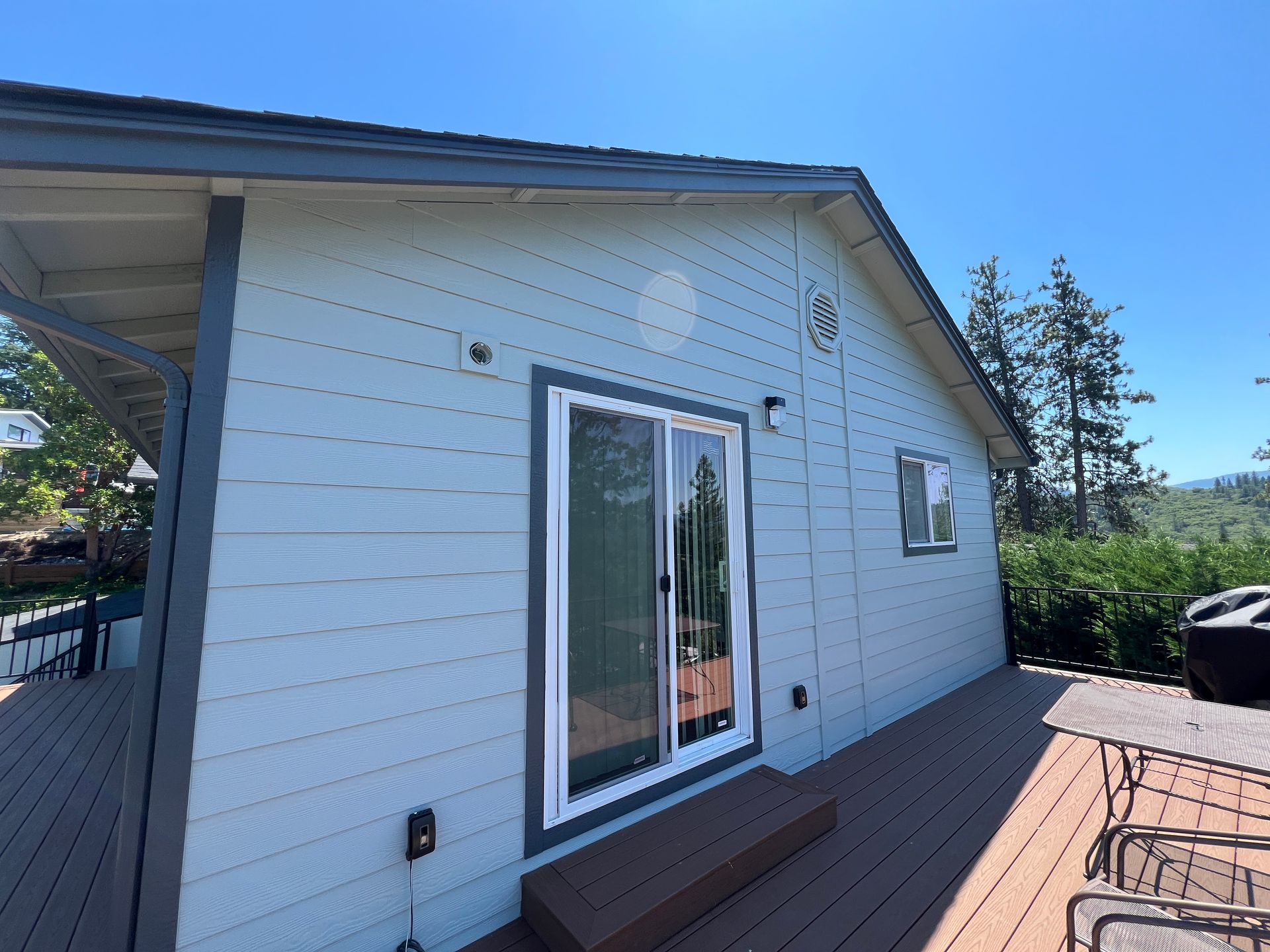Blue house with a deck, sliding glass door, and a sunny blue sky.
