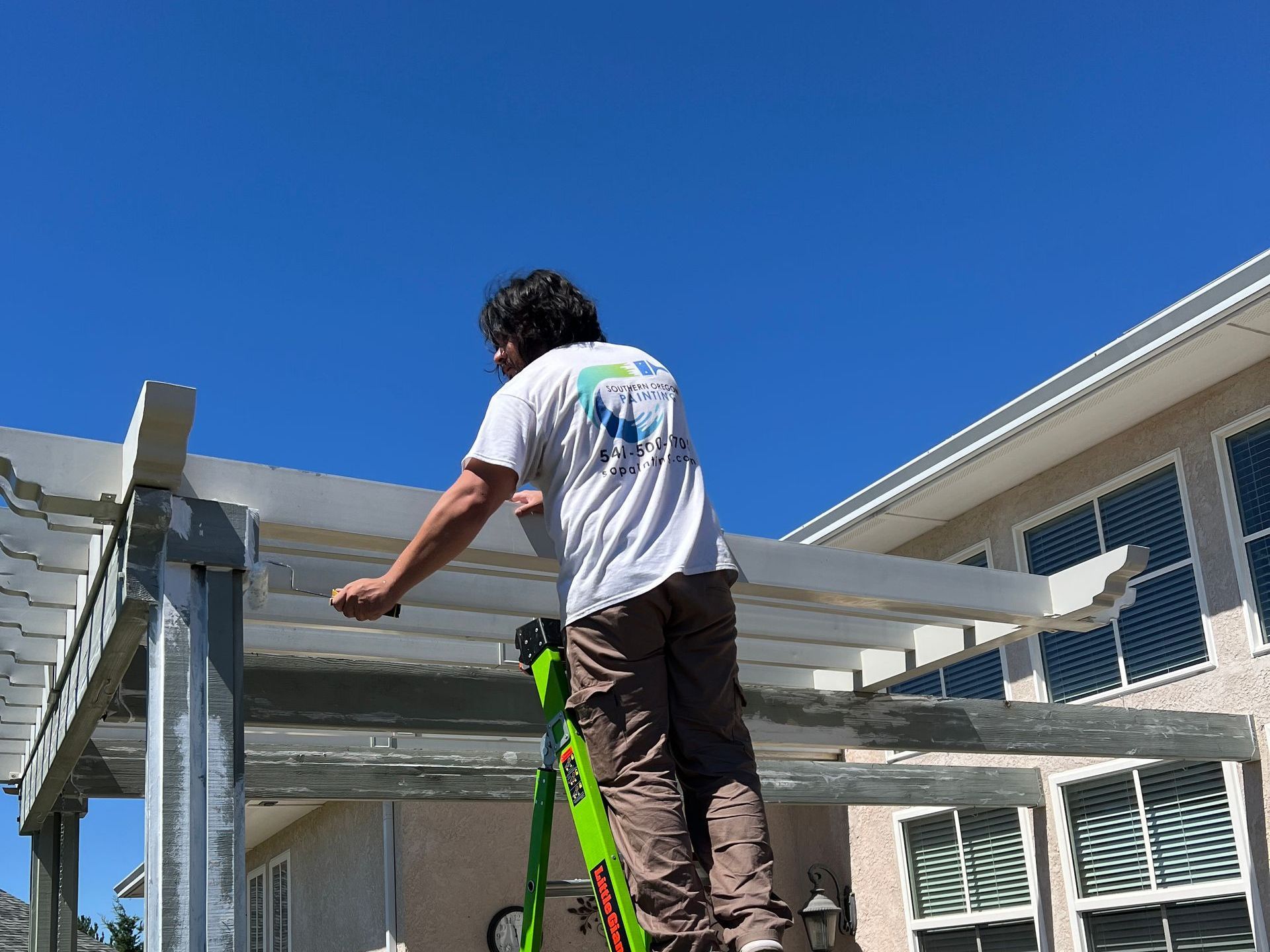 A man is standing on a ladder is painting a pergola