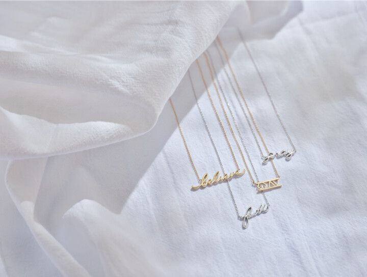 Three necklaces with the word love on them are laying on a white cloth.