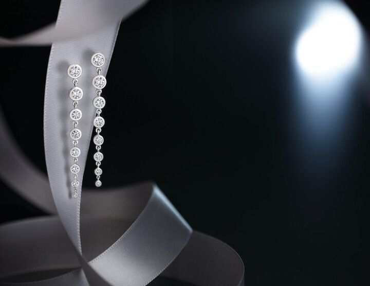 A pair of diamond earrings hanging from a white ribbon