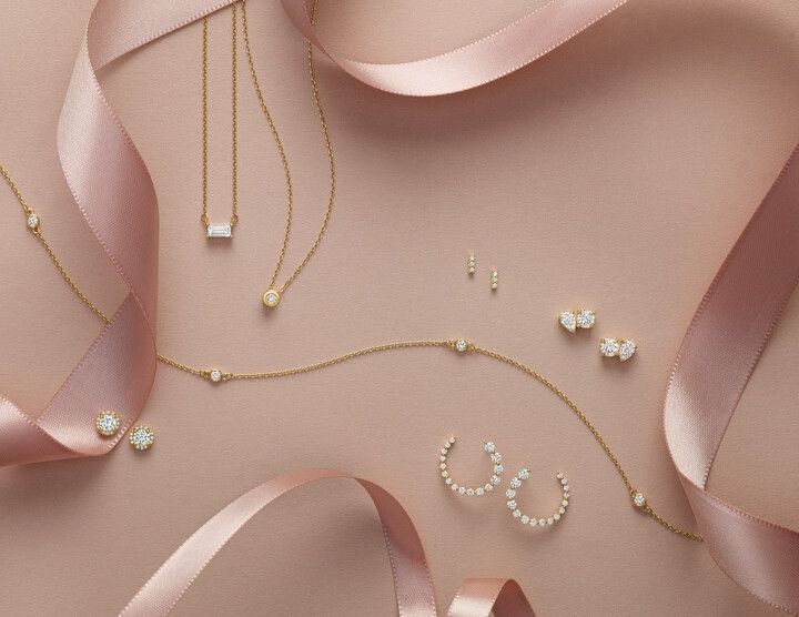 A variety of jewelry is sitting on a pink surface with a pink ribbon.