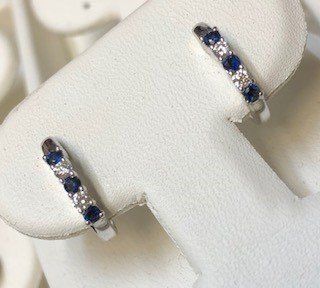 A pair of sapphire and diamond hoop earrings are sitting on a white display stand.