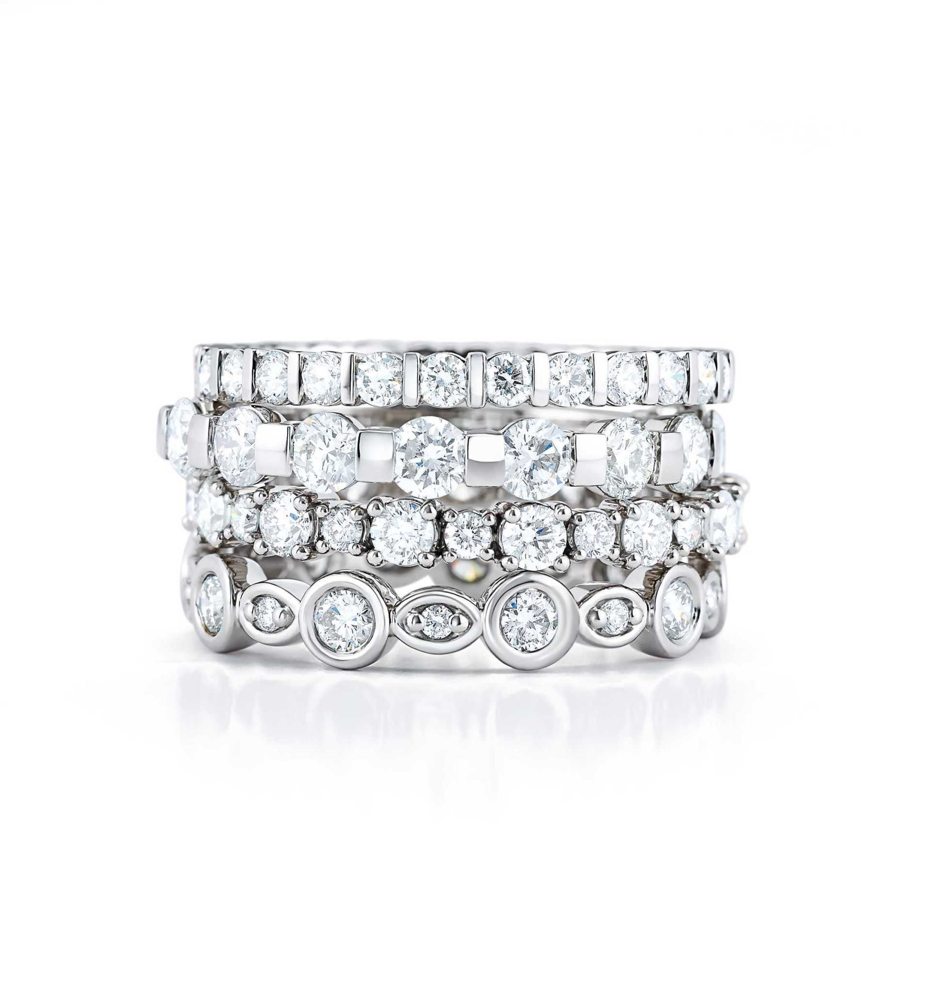 A stack of white gold rings with diamonds on a white surface.