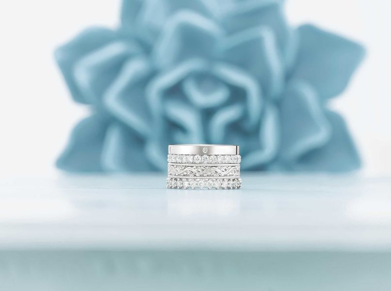 A stack of wedding rings are sitting on a table in front of a blue flower.