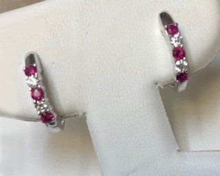 A pair of hoop earrings with rubies and diamonds on a white surface.
