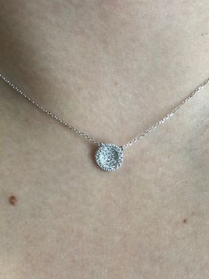 A woman is wearing a necklace with a round pendant on her neck.