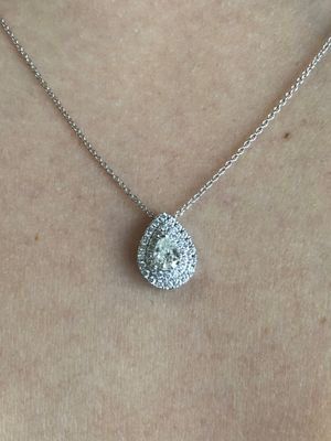 A woman is wearing a necklace with a pear shaped diamond pendant.