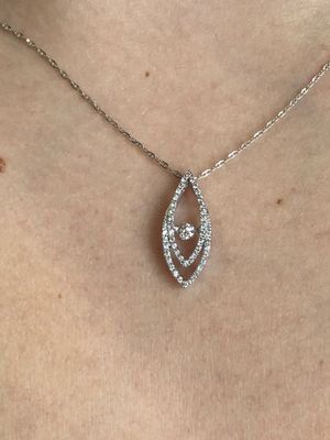A woman is wearing a necklace with a diamond pendant on her neck.