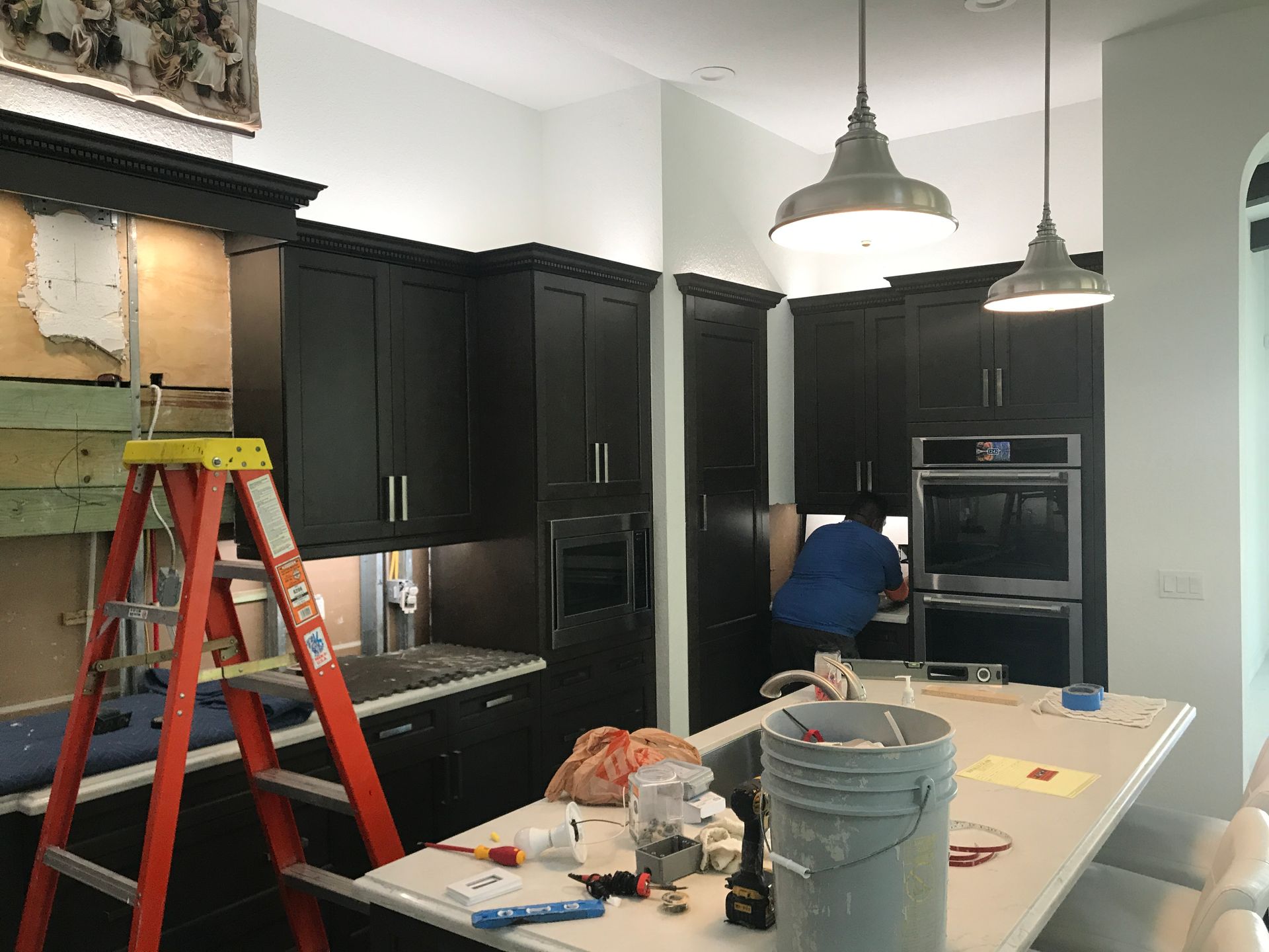 Technician performing electrical installation in custom kitchen remodel with dark cabinetry