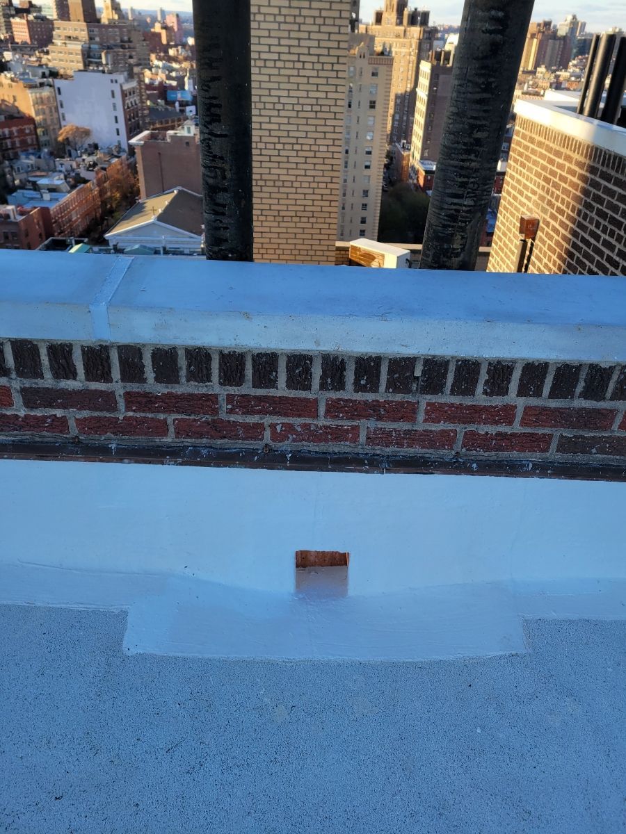 There is a brick wall on the roof of a building with a view of the city.