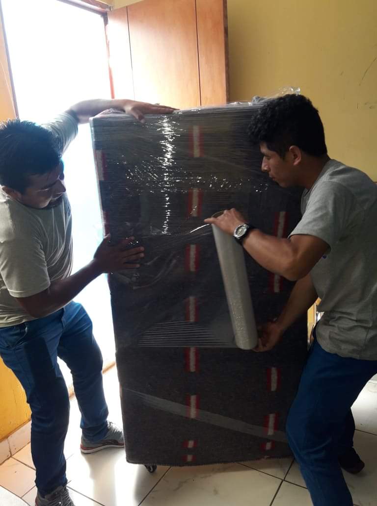 Dos hombres envuelven un gran mueble con film plástico.