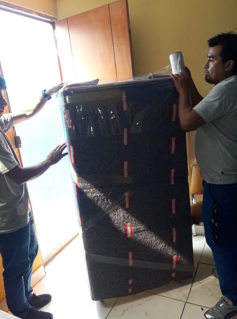 Dos hombres llevan un colchón grande en una habitación