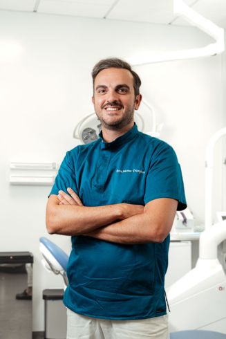 Un uomo in camice medico color verde acqua è in piedi con le braccia incrociate in una luminosa clinica dentistica.