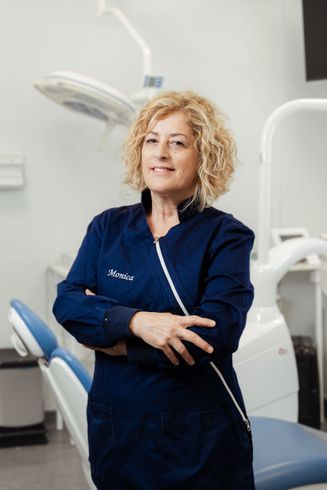 Dentista in camice blu scuro in piedi in uno studio dentistico con attrezzature odontoiatriche alle sue spalle